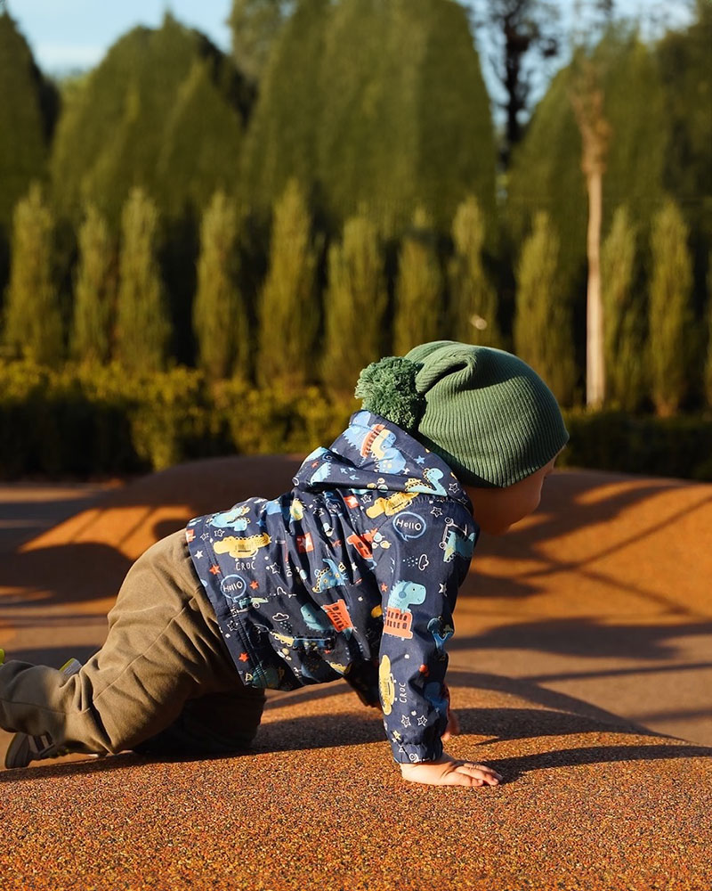 young toddler crolls across a playground surfacing. 